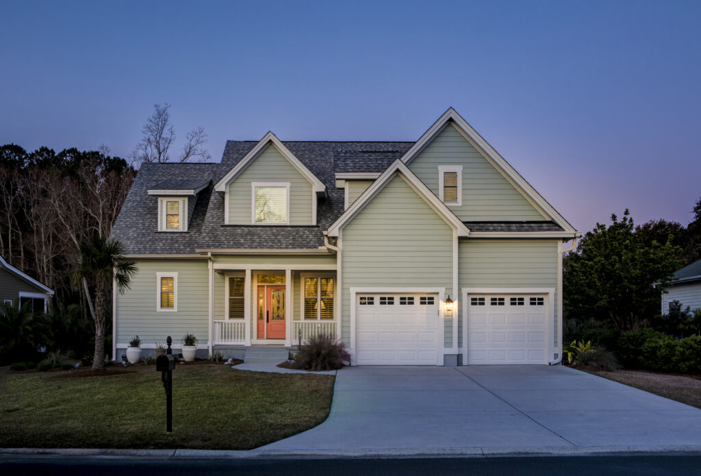 A two-storey light green suburban home with a double garage, taken at dusk with soft lighting and a clear sky.