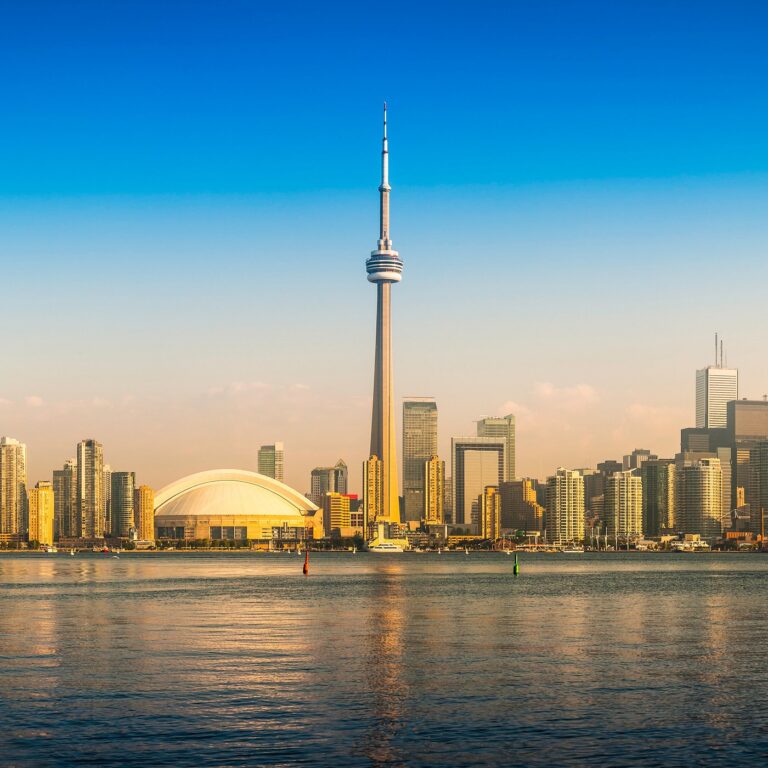 Toronto skyline featuring the CN Tower and Rogers Centre viewed across the water at sunset.