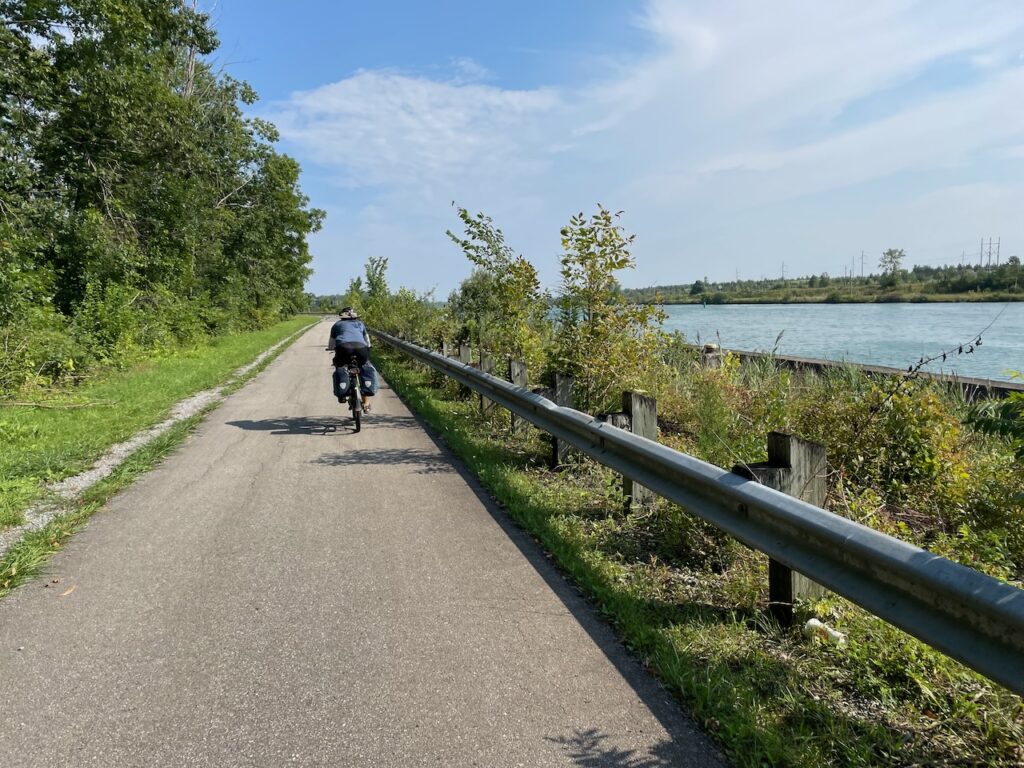 Cyclist riding along the Welland Canal Parkway Trail beside the water on a sunny day in Niagara.