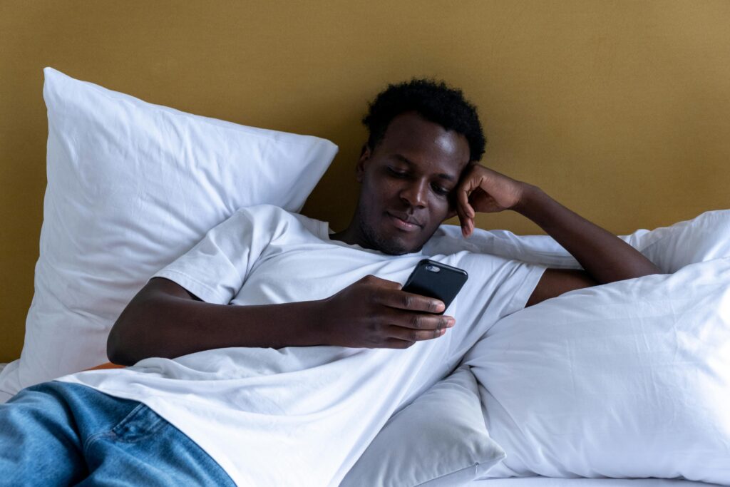 A person lying in bed looking at their phone, representing endless scrolling that can lead to decision fatigue when house-hunting online