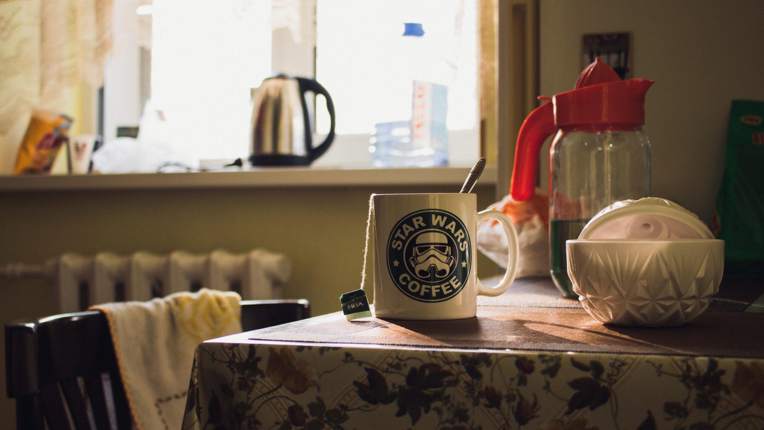A kitchen table in soft morning light with a Star Wars coffee mug, tea bag, and everyday clutter, evoking a lived-in feel of early September routines.