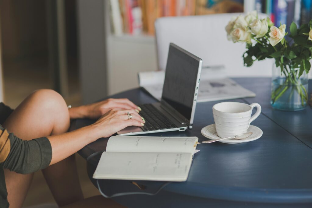 Person working on a laptop at a kitchen table with coffee and a notebook, representing how to find the right home by focusing on life decisions.