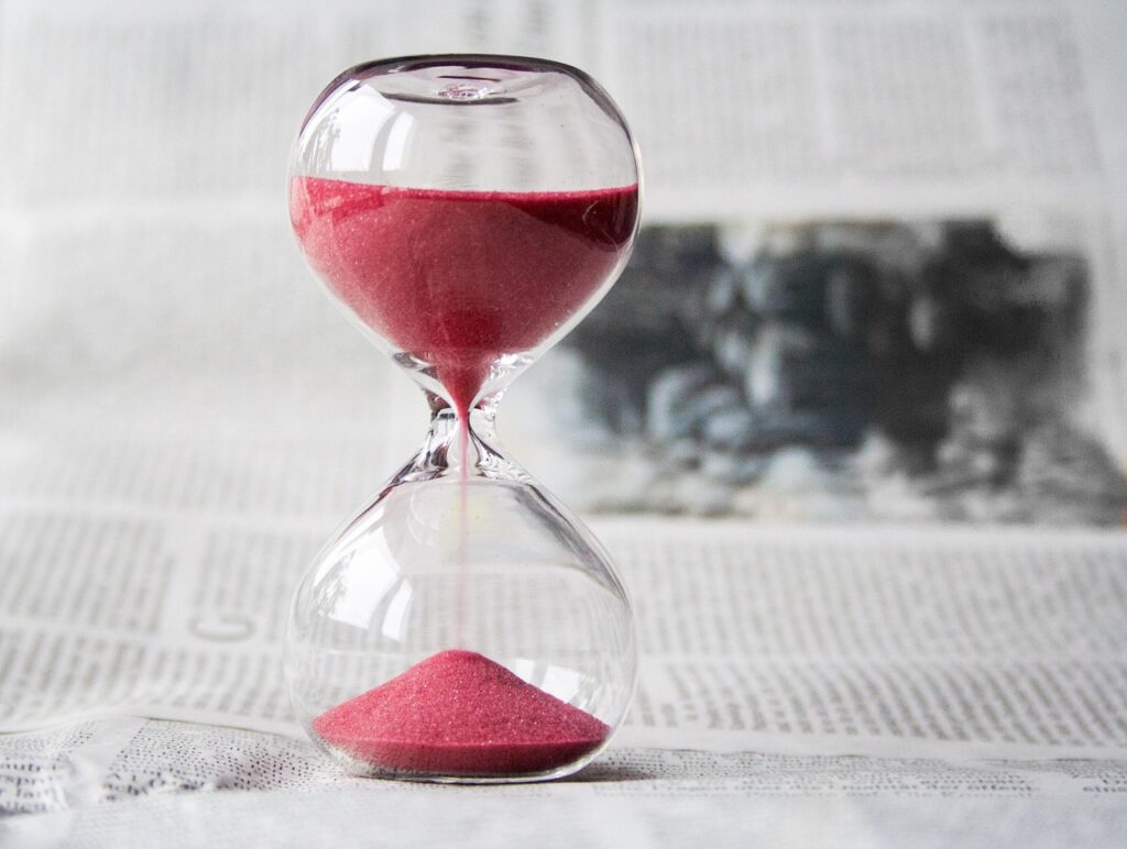 Clear glass hourglass with pink sand flowing, symbolizing the passage of time and waiting.