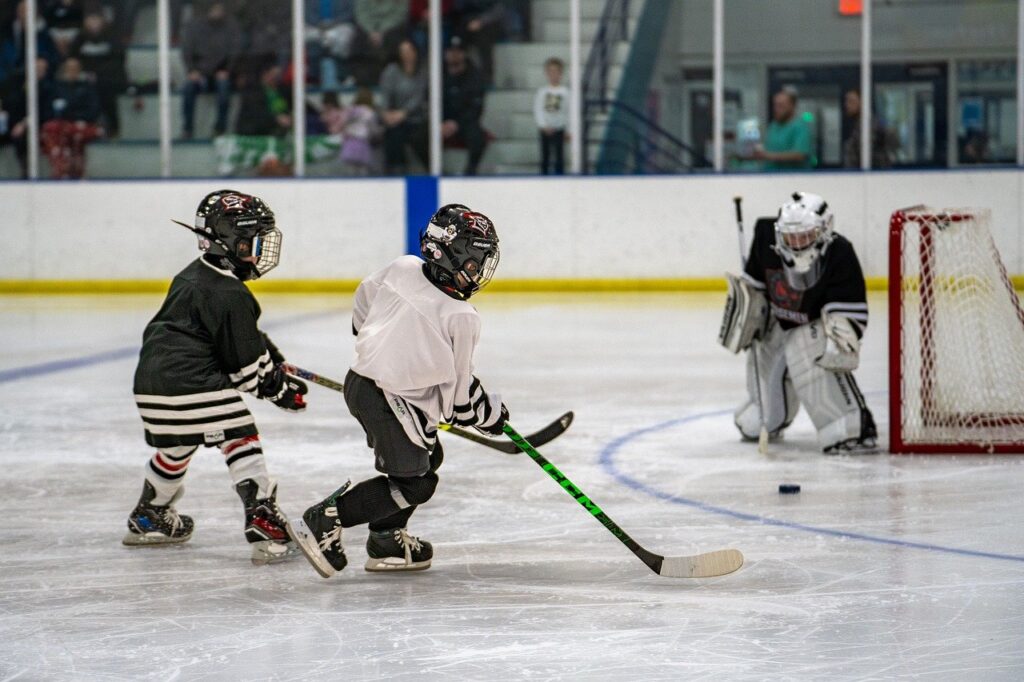 Kids playing ice hockey in a local arena, with a goalie defending the net.